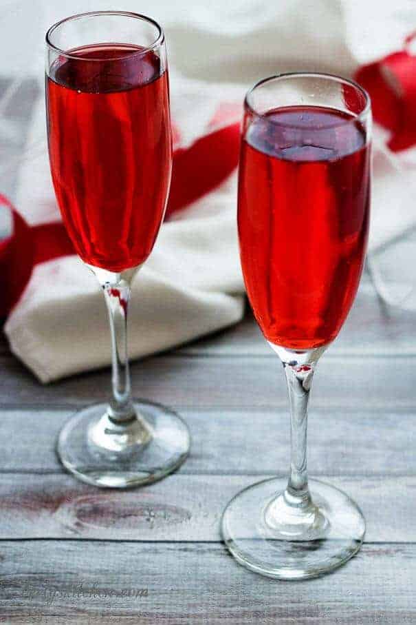 Two glasses of champagne in long stemmed wine glasses with a red ribbon.