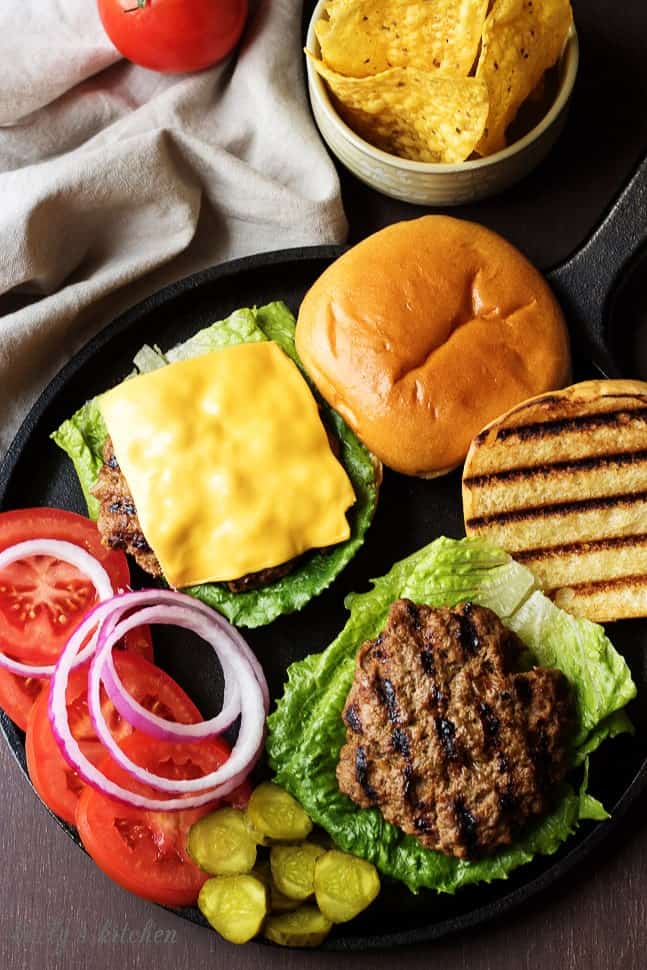 Homemade Hamburgers on buns with toppings laid out.