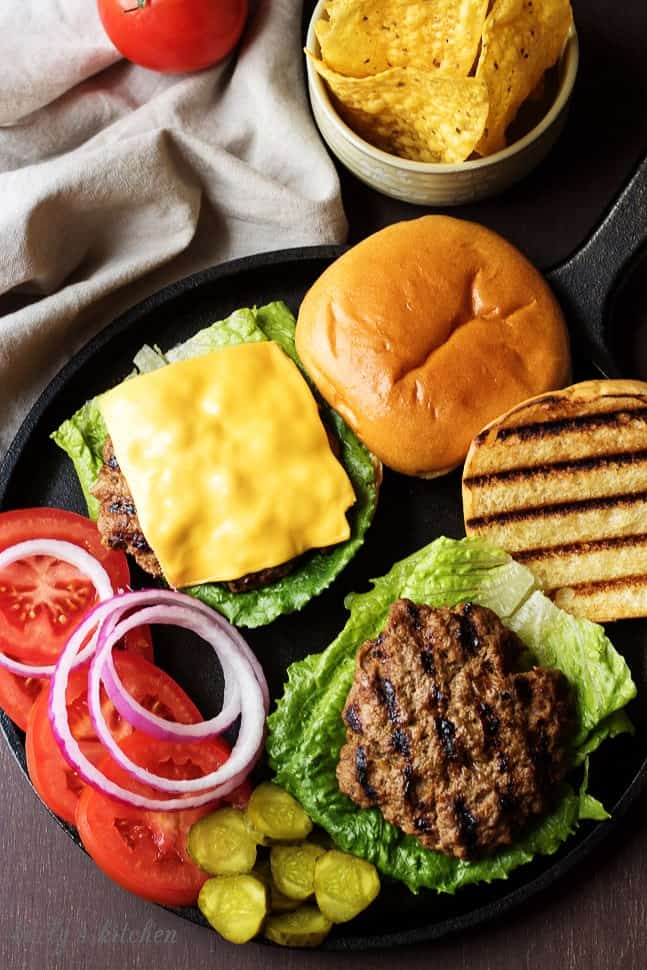 Homemade hamburgers on buns with toppings laid out.