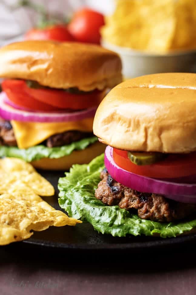 Two juicy hamburgers on a skillet with lots of toppings.