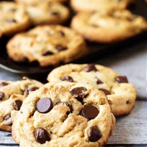 Pile of three peanut butter chocolate chip cookies in front of a pan of cookies.