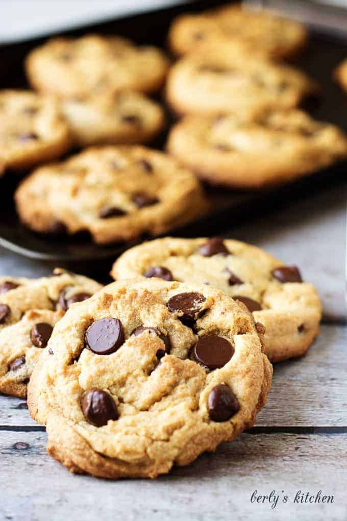 Pile of three peanut butter chocolate chip cookies in front of a pan of cookies.