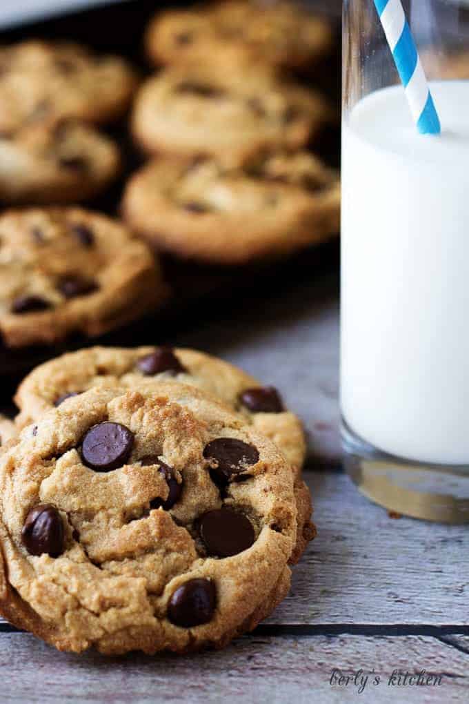 Chewy peanut butter cookies with dark chocolate chips next to a cup of milk.