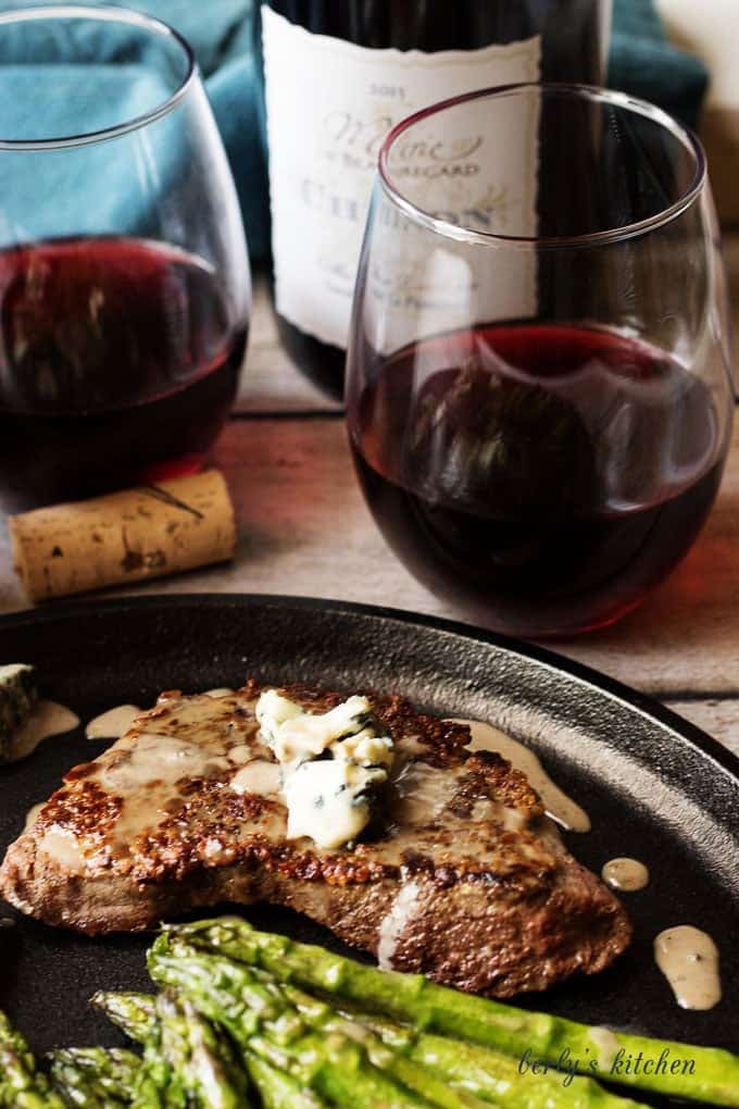 Close up of steak on cast iron with glasses of wine.