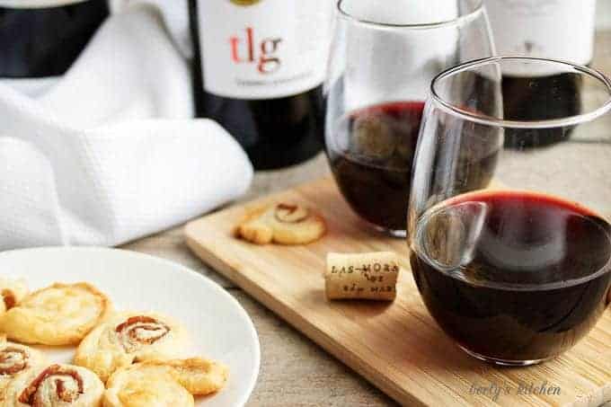 Two glasses of red wine on a cutting board with crackers.