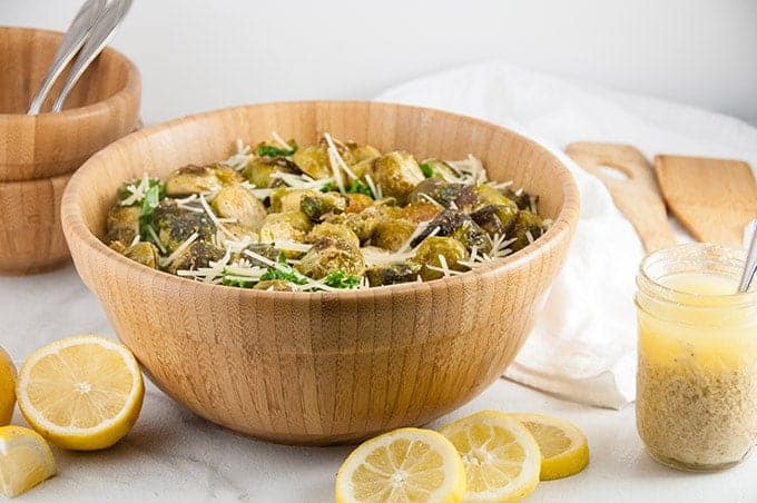 Brussels sprouts salad in a bamboo bowl with lemon slices.