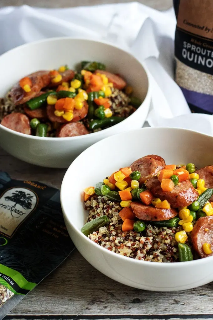 Two white bowls filled with corn, green beans, sausage and quinoa.