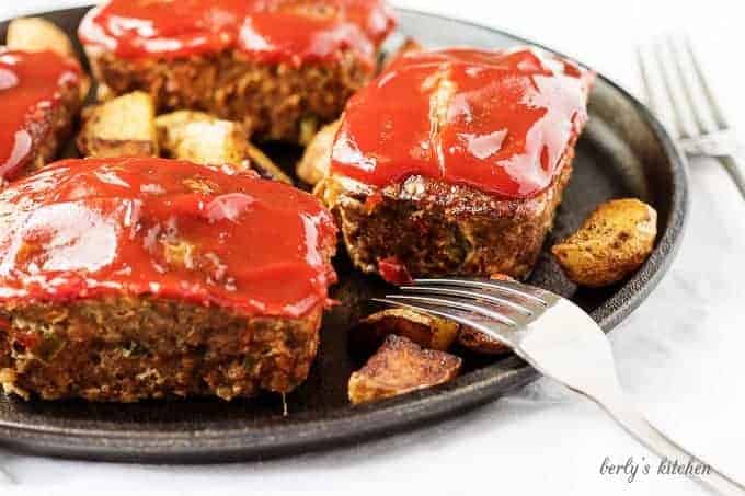 Mini meatloaves topped with ketchup next to two forks.
