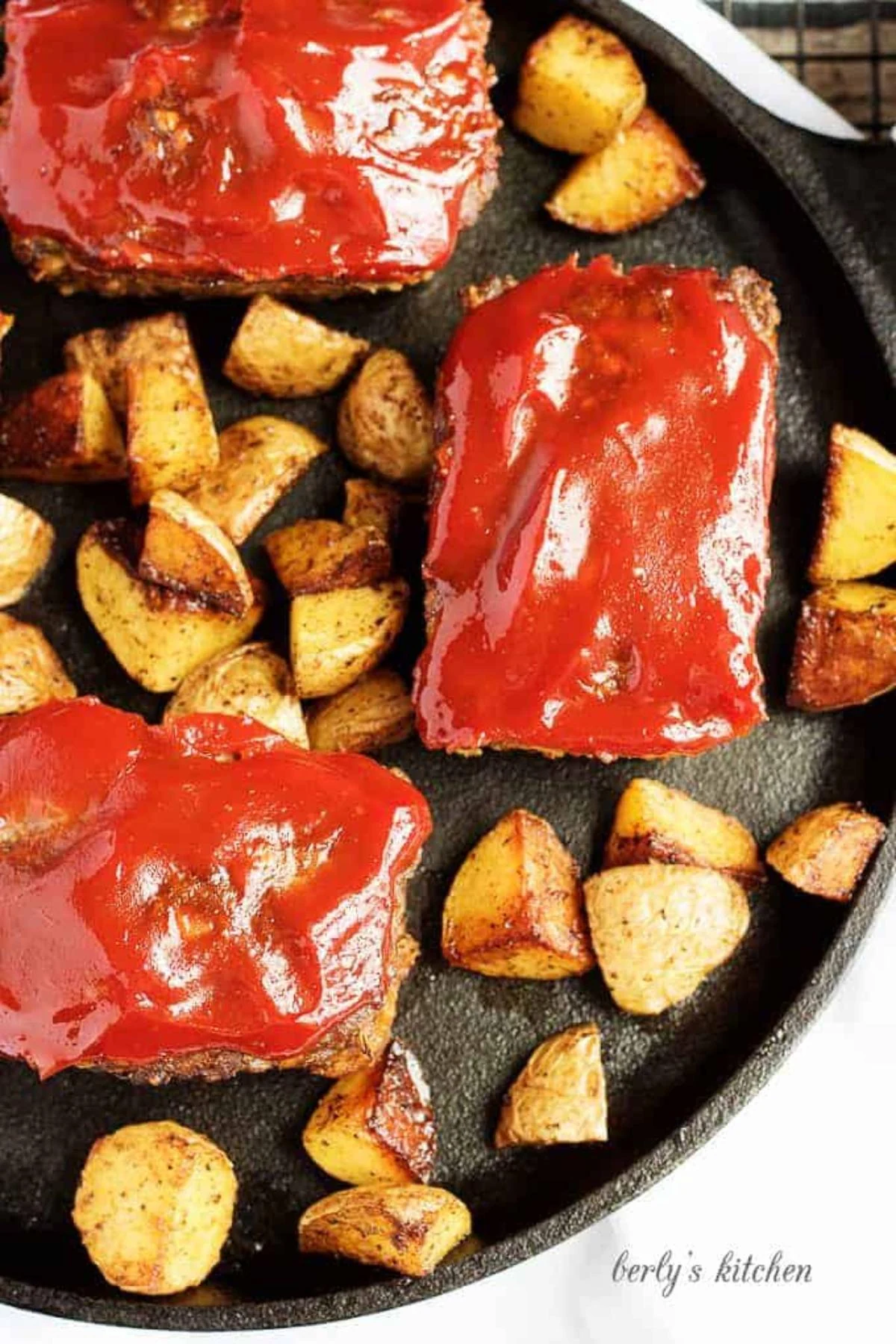Top down view a multiple mini meatloaves surrounded by several seasoned potatoes.