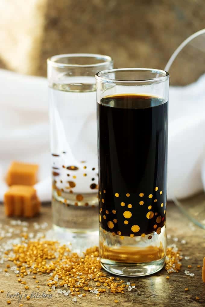 Coffee liqueur and gin in shot glasses with gold and white decorating sugar.