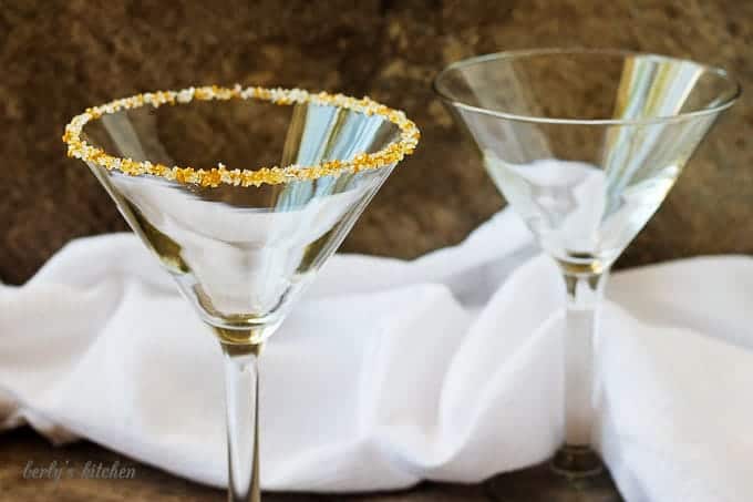 Two empty martini glasses, one rimmed with gold and white sugar.