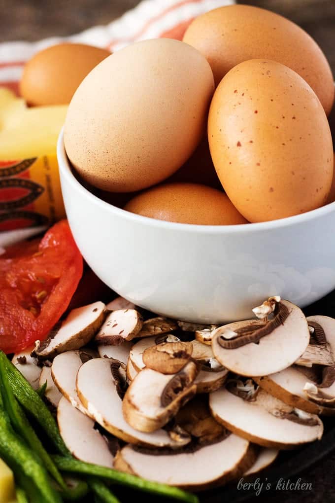 A white bowl filled with brown eggs. The bowl is surrounded by the sliced veggies.