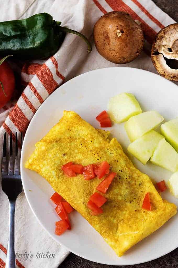 A top-down view of the dish with the omelet and melon chunks. Omelet is garnished with diced tomato.