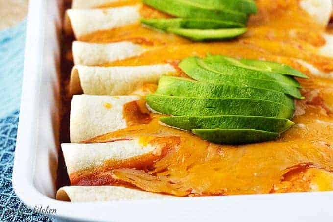 The cooked chorizo enchiladas covered in cheddar cheese, sauce, and sliced avocado.