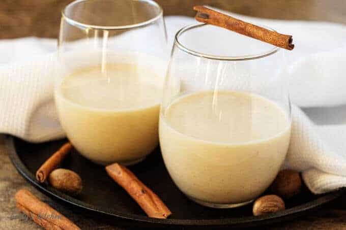 Two small glasses half-filled with coquito garnished with cinnamon and nutmeg.