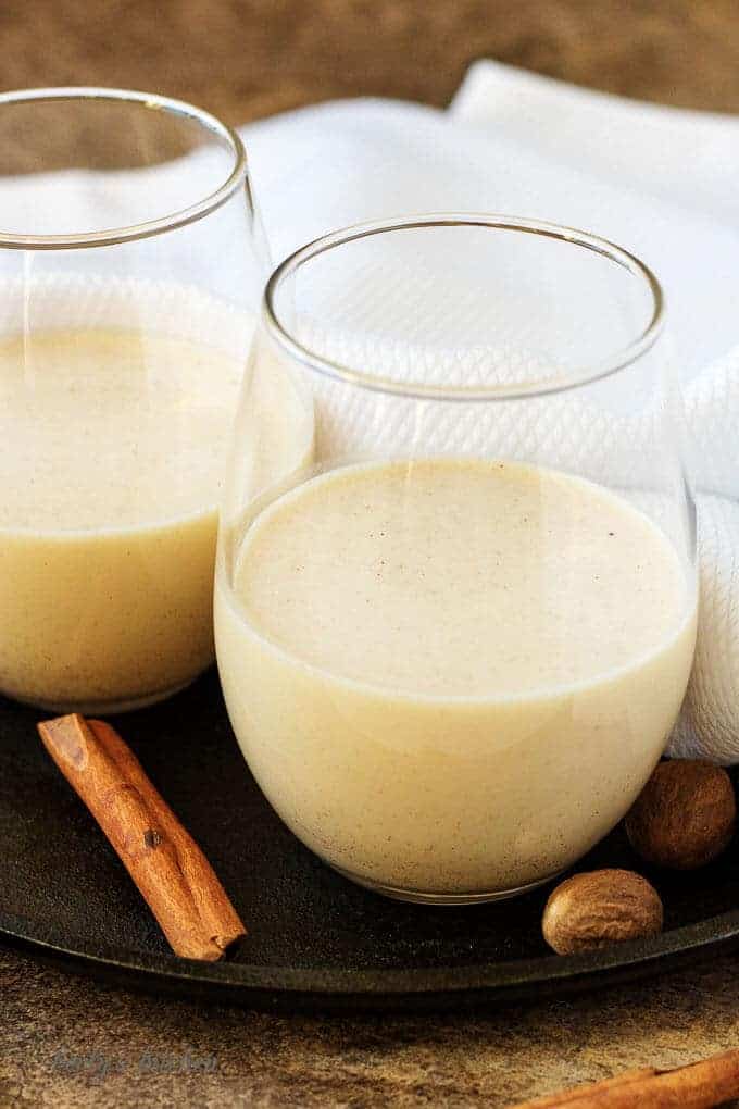 Two glasses half filled with coquito, chilled and ready to serve with cinnamon.