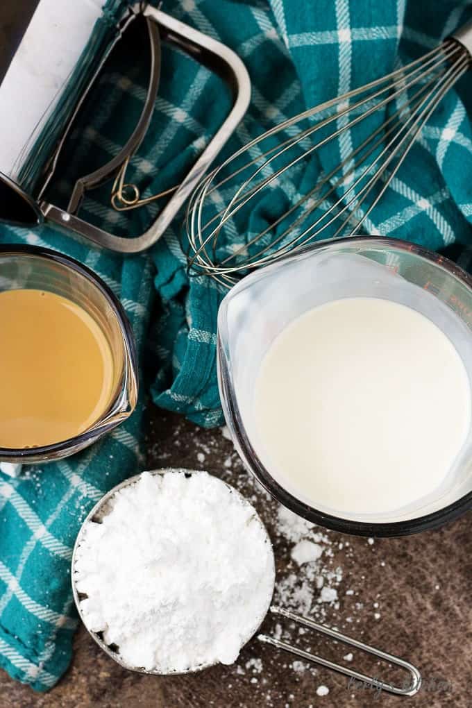 Top down shot of a sifter, whisk, irish cream liqueur, powdered sugar, and heavy cream used to make irish cream flavored whipped cream.