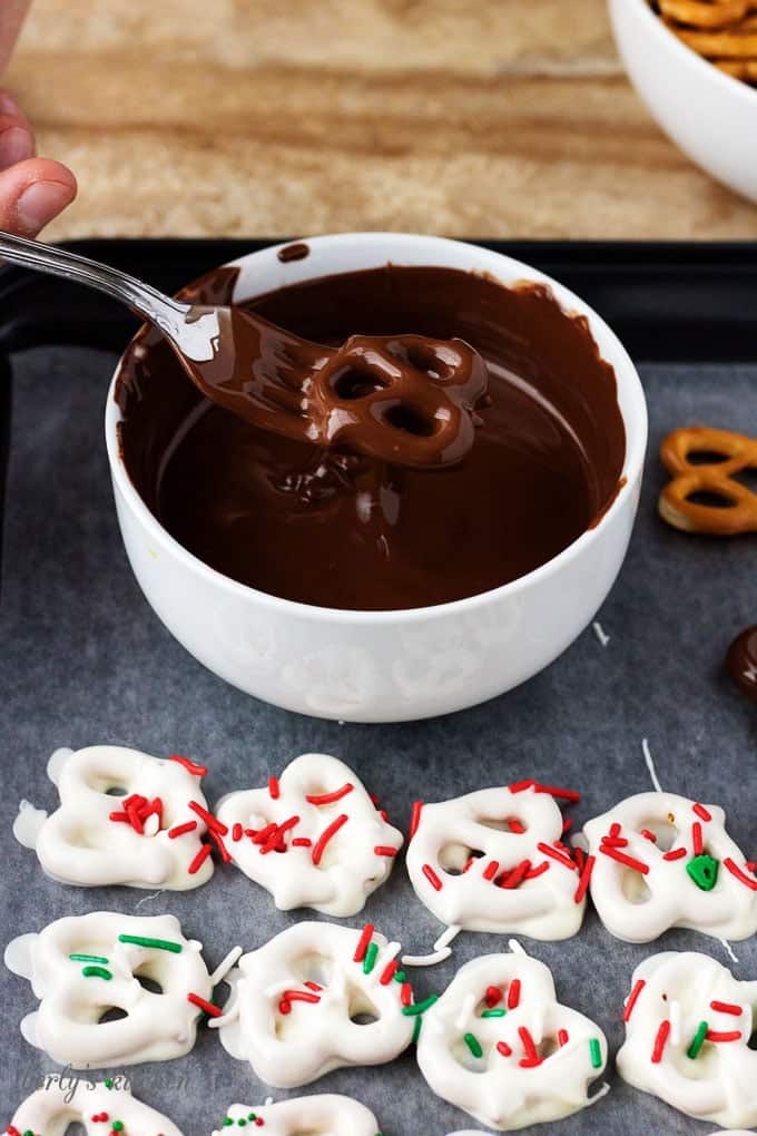 Side-view of the chocolate covered pretzels being dipped in melted dark chocolate with a fork.