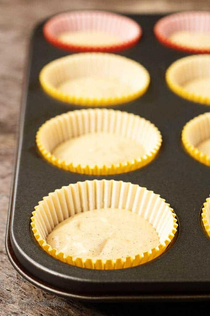 A side-view of the colorful cupcake liners in a cupcake pan half-filled with batter.