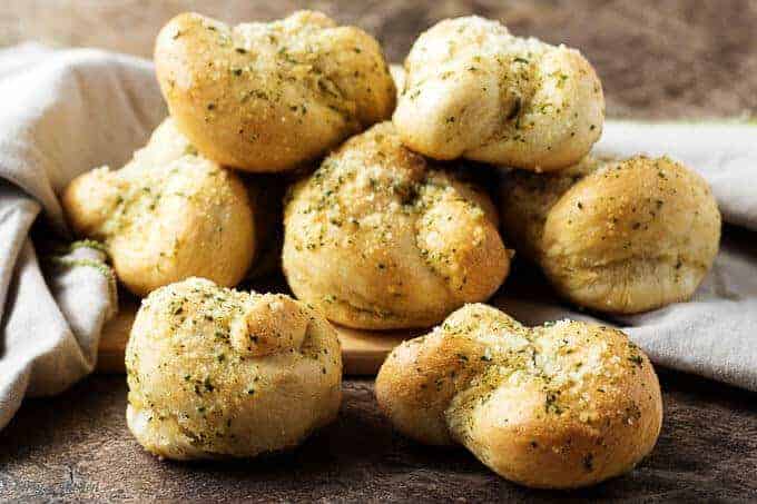 The finished garlic knots recipe showing the garlic butter topped knots stacked on cutting board.