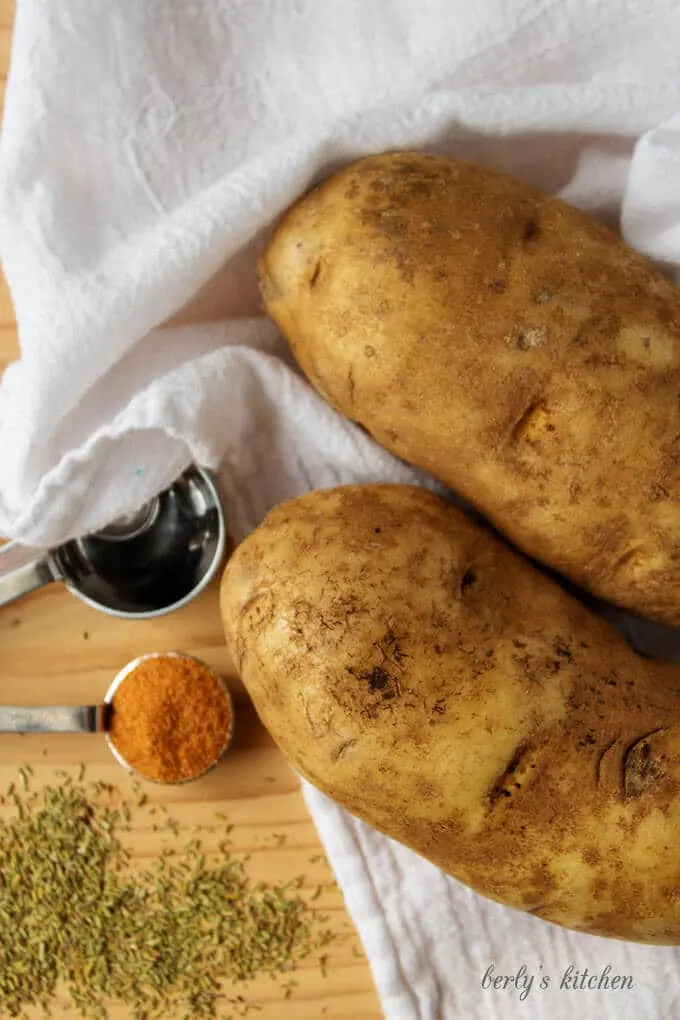 The potatoes, season salt, and rosemary, on a cutting board with a white towel.