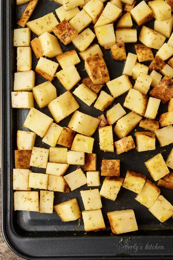 The home fries have been spread out evenly on a dark sheet pan for baking.