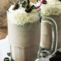 Two Oreo milkshakes in chilled mugs with whipped cream and cookies toppings .