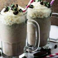 A side-view of two Oreo milkshakes in mugs, topped with whipped cream, and crumbled cookies.