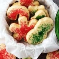 The sugar sprinkled cookies, cut into holiday shapes like trees and snowmen, in a cookie tin.