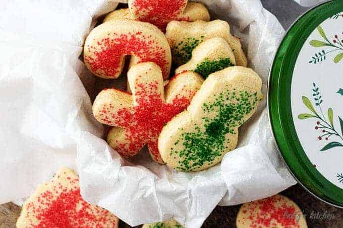 The sugar sprinkled cookies, cut into holiday shapes like trees and snowmen, in a cookie tin.
