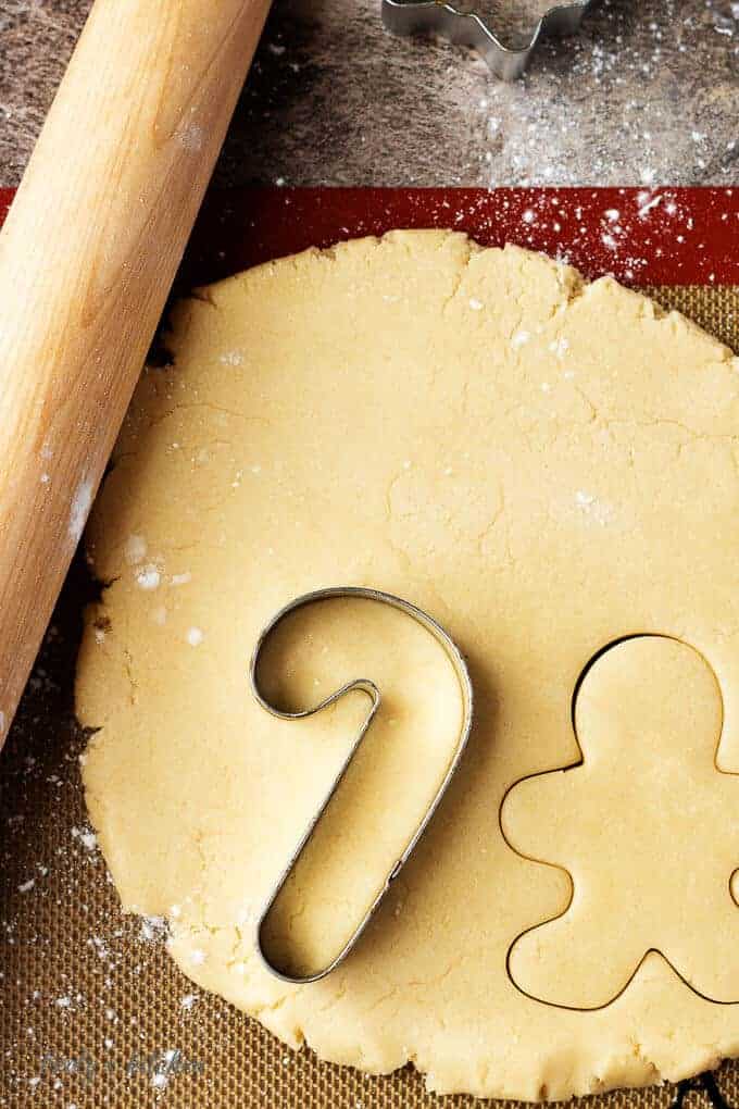 The rolled out dough being cut into fun holiday shapes like candy canes and ginger men.