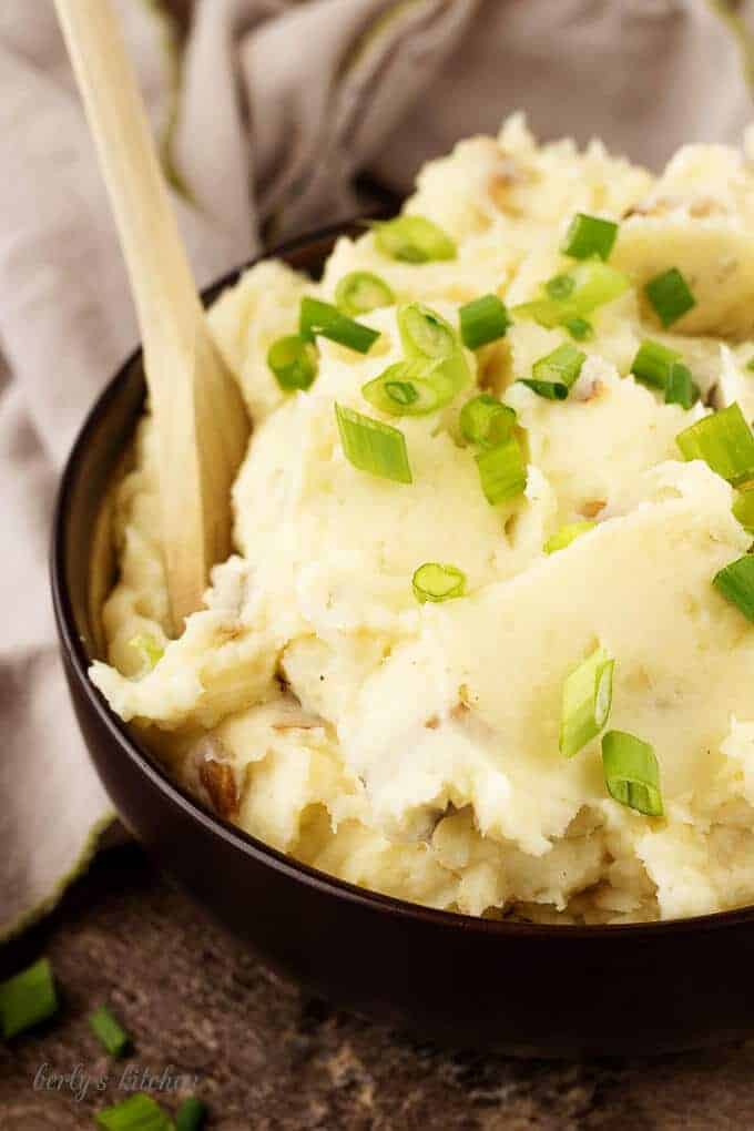 A close-up photo of the finished parmesan mashed potatoes in a brown serving bowl.