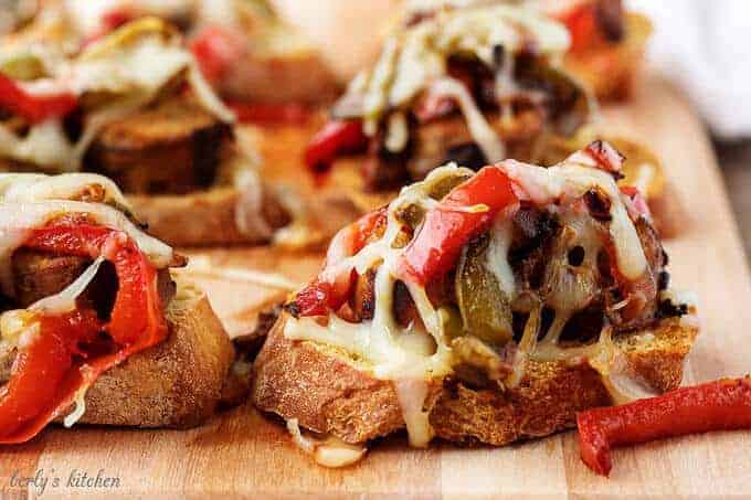 A close-up photo of the finished recipe for sausage and peppers crostini on a cutting board.