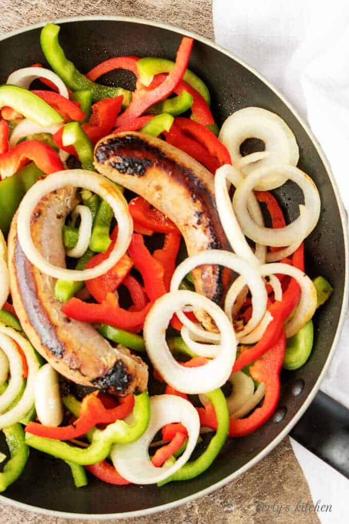 Top-down shot of the sausage and peppers cooking in large saute pan.