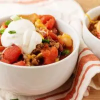 The three bean chili in a white bowl, topped with green onions and sour cream.