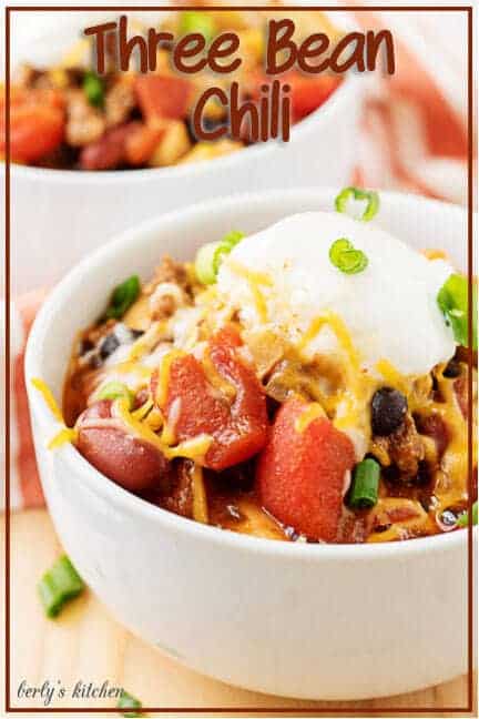 The finished three bean chili in a white bowl garnished with cheese and sour cream.