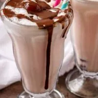A final shot of the finished chocolate covered cherry milkshakes in glasses with straws and smothered with chocolate sauce.