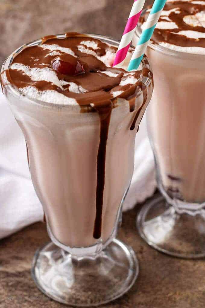 A final shot of the finished chocolate covered cherry milkshakes in glasses with straws and smothered with chocolate sauce.