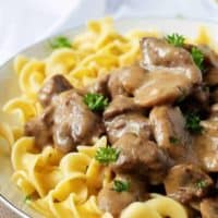 Close up of beef stroganoff on a white plate with a white napkin in the background.