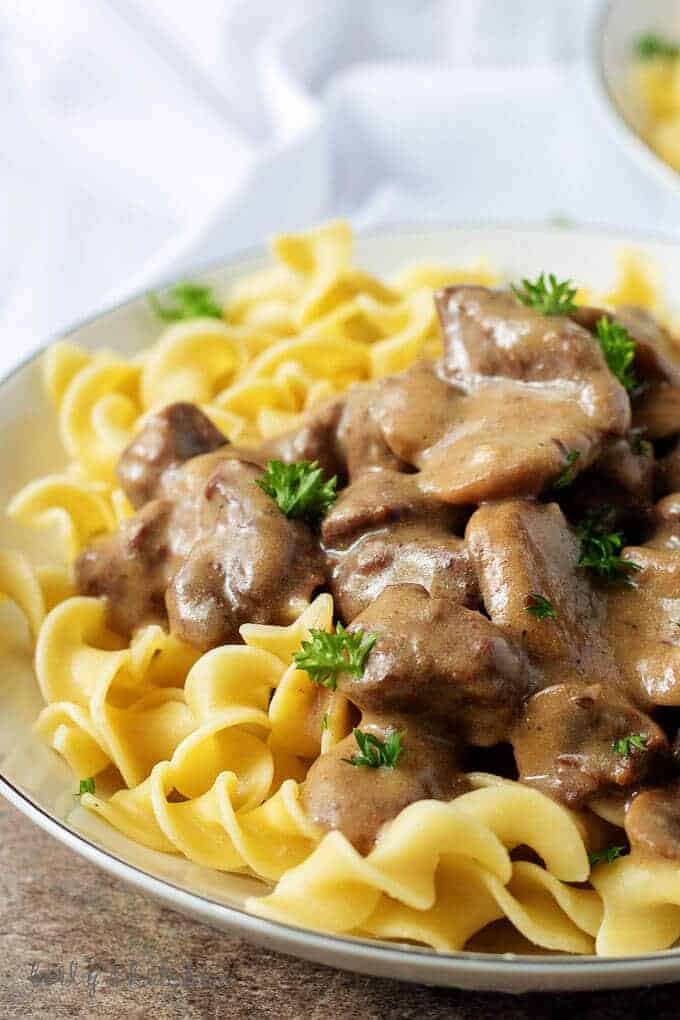 Close up of beef stroganoff on a white plate with a white napkin in the background.