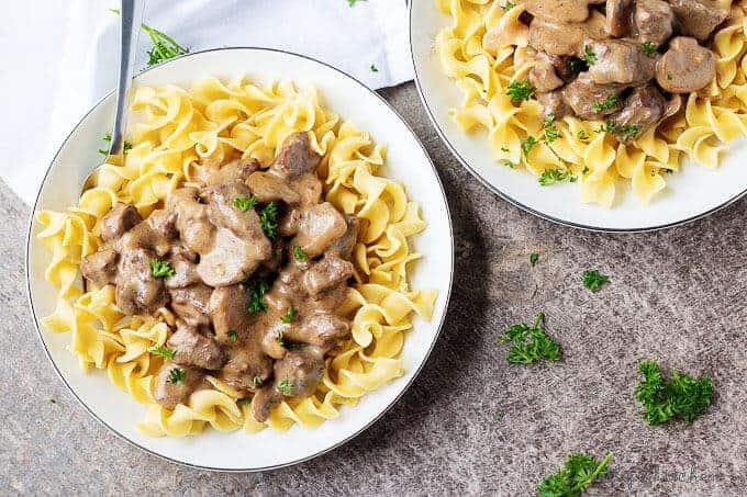 Ariel view of two plates of easy beef stroganoff next to scattered parsley.