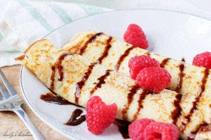 The finished gluten free crepes, on a plate, garnished with raspberries.