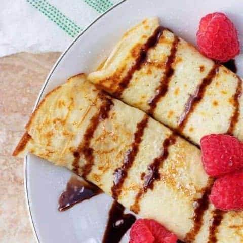 Gluten Free Crepes With Raspberry Filling The finished gluten free crepes with raspberry filling on a plate drizzled with chocolate syrup.