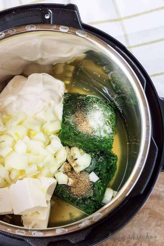 Ariel view of cream cheese, spinach, sour cream, garlic, onions, salt, pepper, and chicken broth in an instant pot.