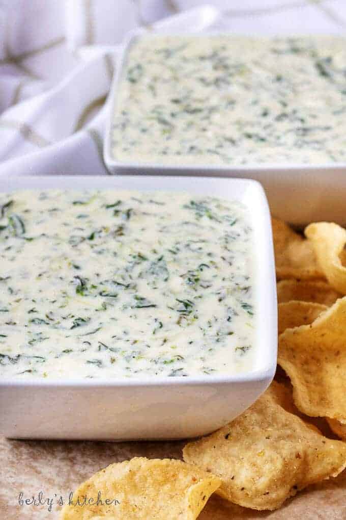 Front view of hot spinach dip in white bowls surrounded by chips.