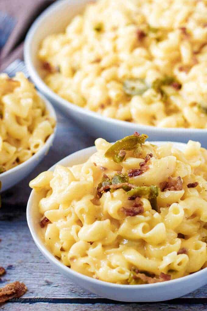 Close up of a bowl of instant pot mac and cheese topped with bacon and jalapenos with two additional bowls in the background.