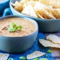 Bowl of hamburger dip next to a bowl of tortilla chips and scattered chips.