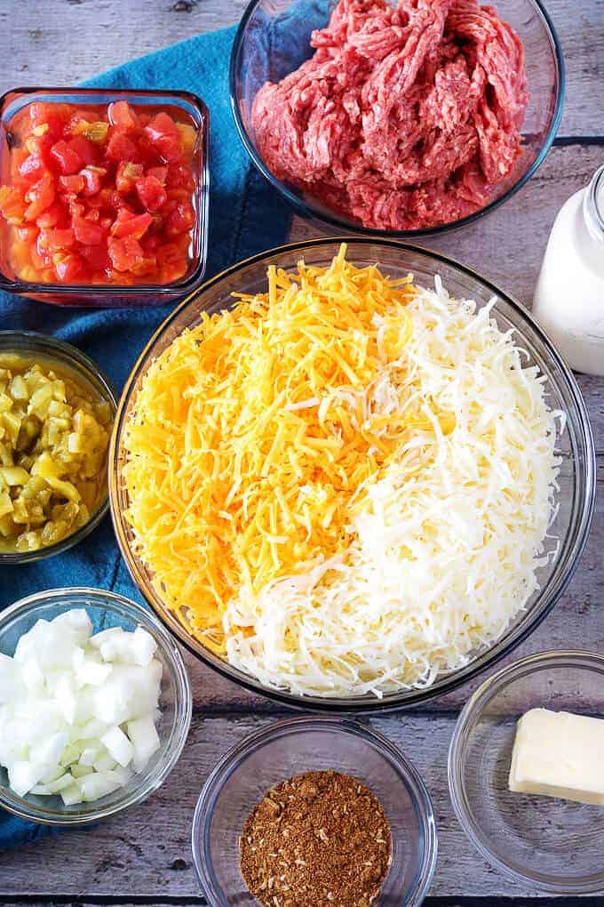 Ariel view of cheese, tomatoes, ground beef, taco seasoning, onions, and green chiles used in hamburger dip.