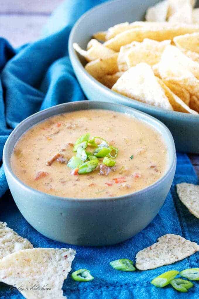 Hamburger dip in a blue bowl next to tortilla chips and green onions.