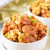 Close up view of sausage and chicken jambalaya in two white bowls with scattered green onions.